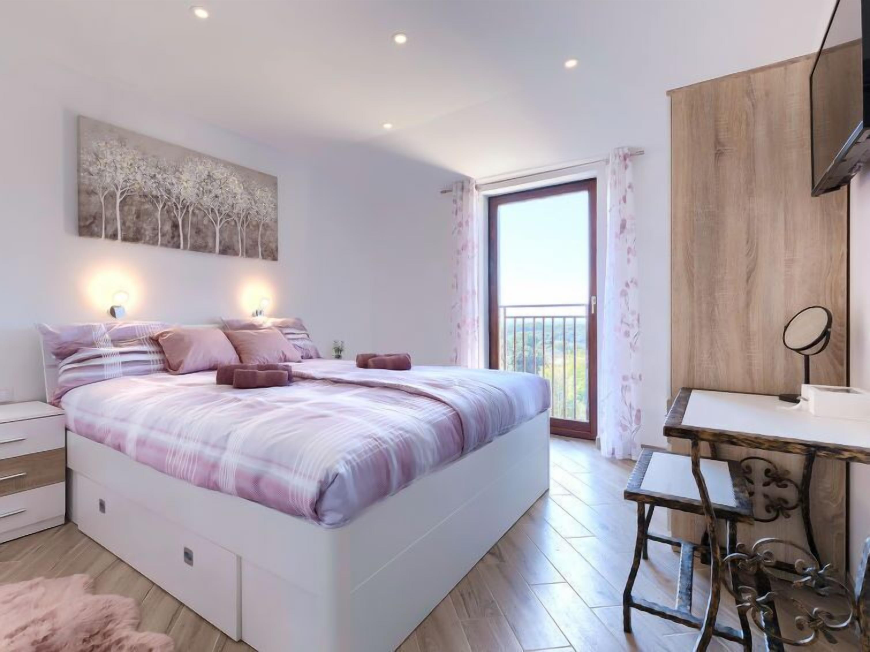 Quarto com cama, mesas de cabeceira, escrivaninha e varanda.