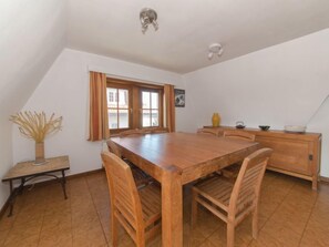A dining area with a wooden table and chairs, a small side table with a vase, and a window with curtains.