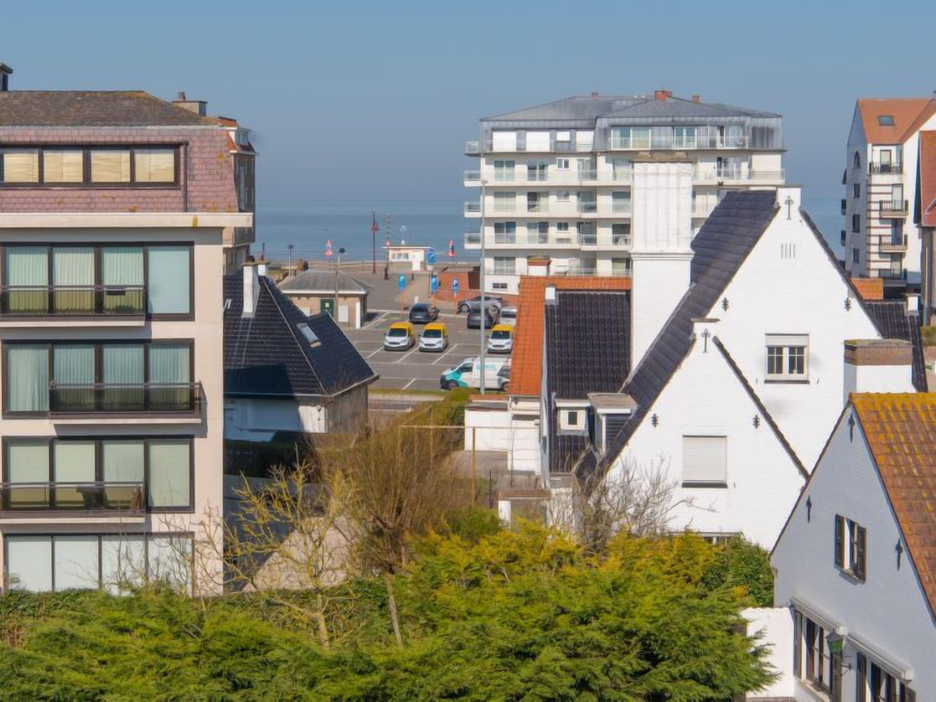 Una zona residencial costera con edificios modernos, una carretera visible y coches estacionados.