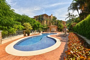 A swimming pool with a curved design, surrounded by a brick walkway and lush greenery. - Bella Vista 2D 3 bdrs pool view in Los Suenos (Playa Herradura)