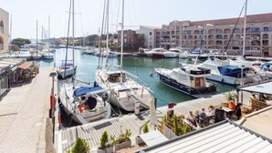 Un puerto deportivo con varias embarcaciones amarradas, un restaurante frente al mar y un edificio con balcones al fondo.