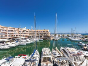 Marina com vários barcos atracados, um edifício com varandas e céu azul límpido.