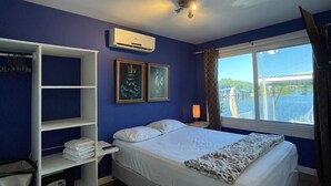 A bedroom with a bed, a wardrobe, an air conditioning unit, and a window with a view of a body of water. - Casa Moon in best neighborhood! (Utila)