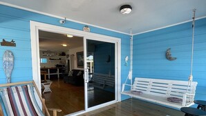 A room with a wooden floor, a striped hammock chair, a white bench with a rope swing, and a small white table with a bowl. - Casa Moon in best neighborhood! (Utila)
