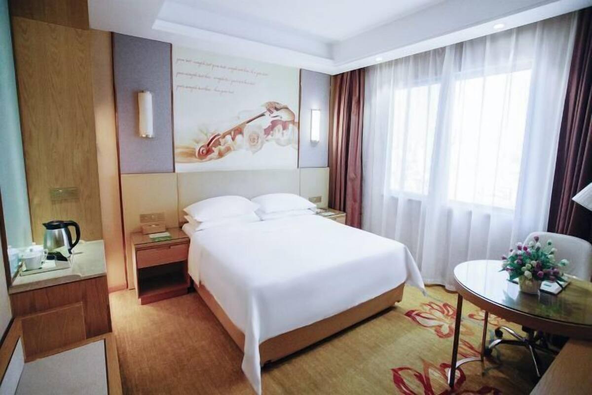 Hotellihuone, jossa on sänky, yöpöytä, lamppu ja näkymä ulos.
