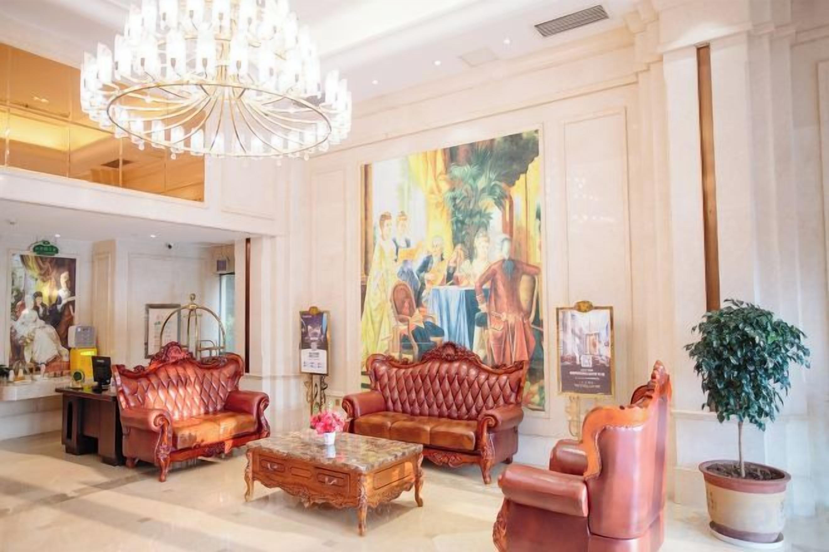 A lobby with a chandelier, red sofas, a coffee table, and a large painting on the wall.