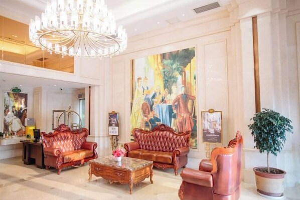 A lobby with a chandelier, red sofas, a coffee table, and a large painting on the wall.