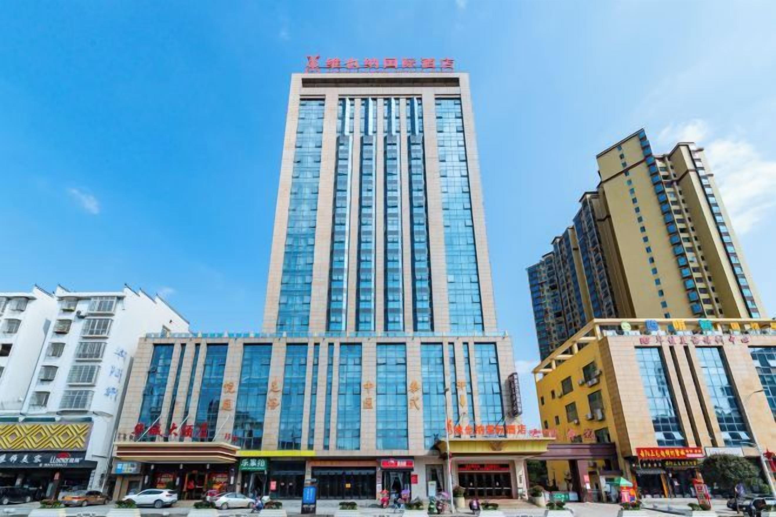 A multi-story hotel with a prominent vertical sign, several ground-level commercial establishments, and a clear blue sky.