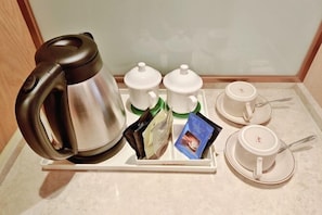 A coffee station with a kettle, two teapots, a tray with tea bags and a magazine, and two cups with saucers.