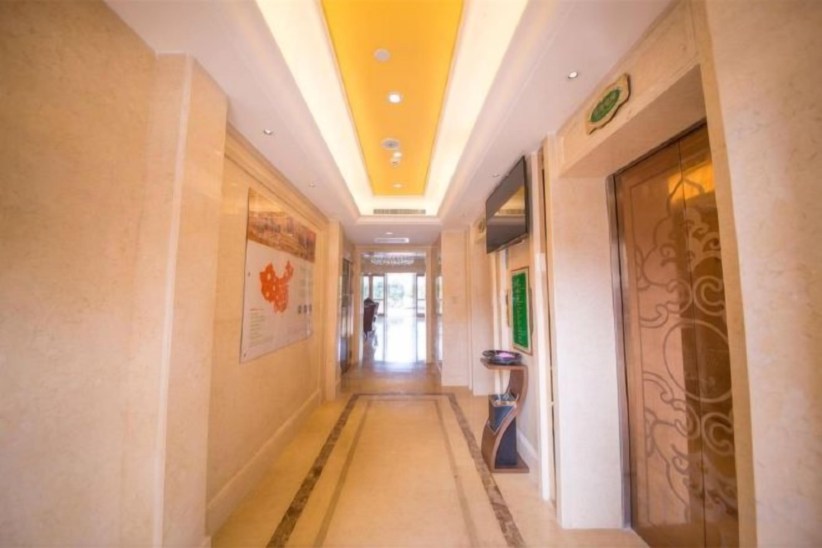 A hotel corridor with a tiled floor, a ceiling with recessed lighting, and a door with a decorative glass panel.