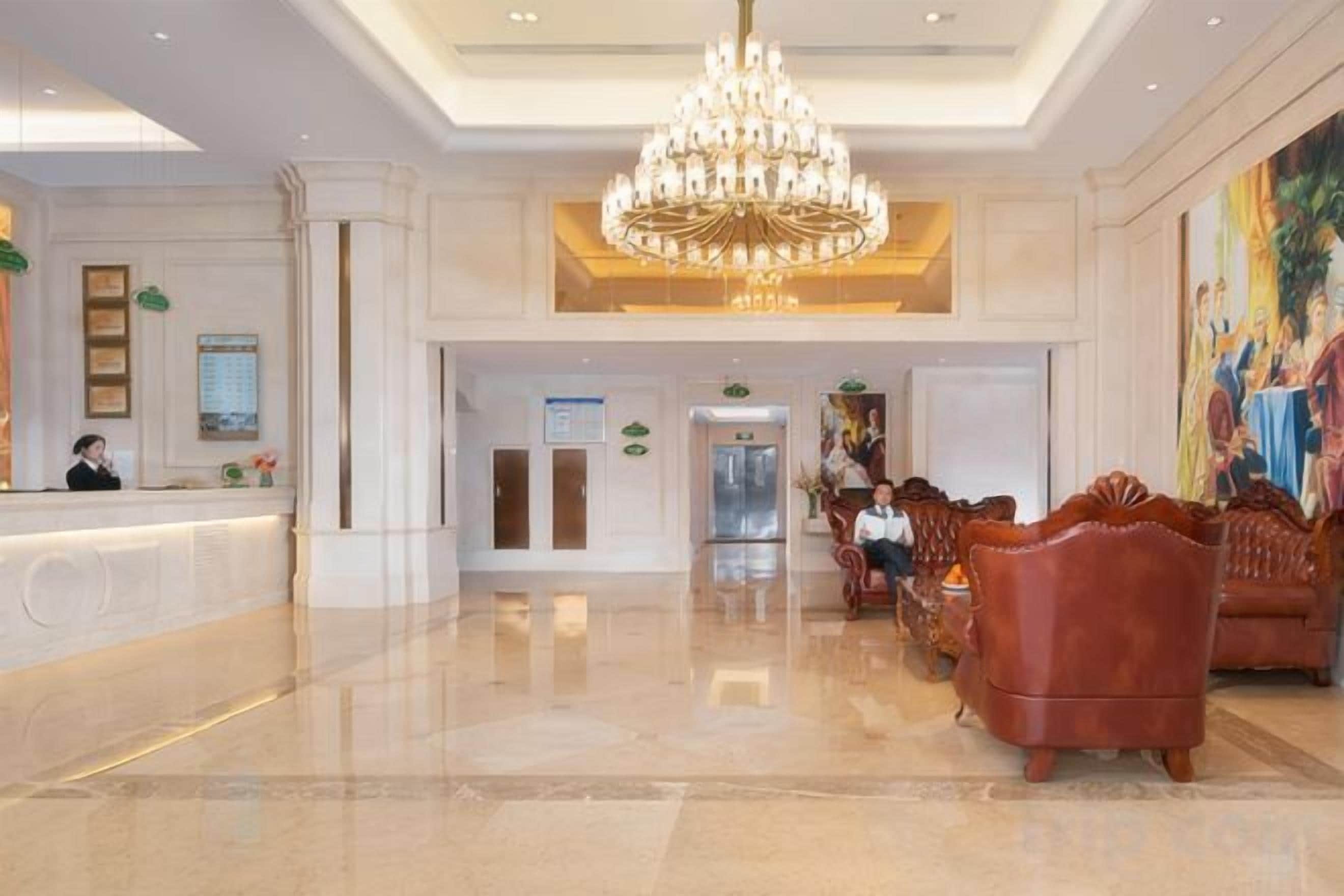 A hotel lobby with a reception desk, a chandelier, seating area, and a painting on the wall.