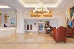 A hotel lobby with a reception desk, a chandelier, seating area, and a painting on the wall.