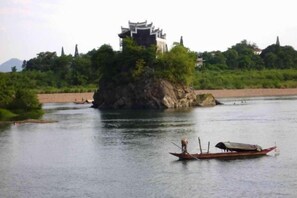 A river with a traditional boat and a building on a small island. - Vienna International Hotel (Yongzhou Lingling Junyue Huacheng) (Yongzhou)