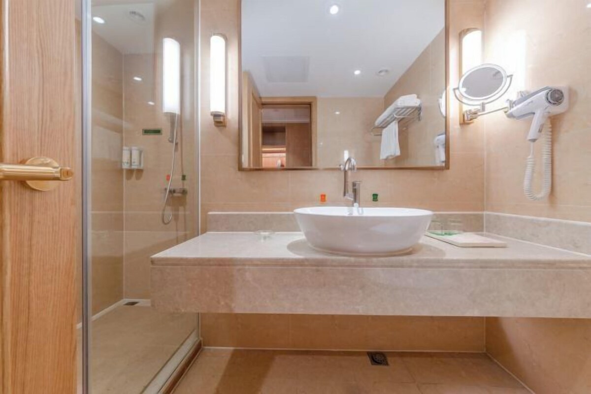 A modern bathroom with a white sink, a mirror, a hairdryer, and a glass shower enclosure.