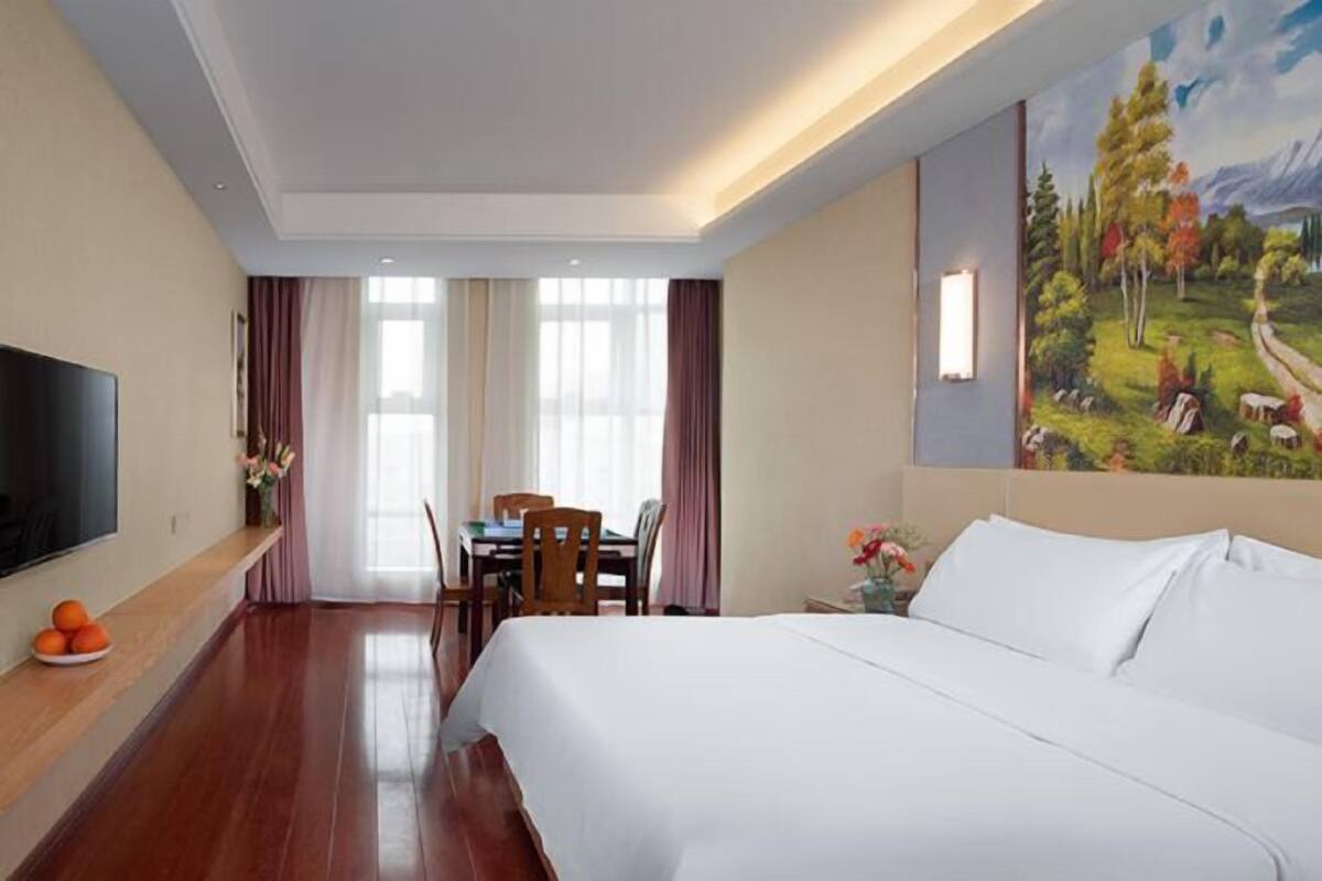 Hotellihuone, jossa on sänky, televisio, ruokapöytä tuoleineen ja seinällä taulu.