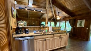 Het interieur van een houten chalet met een keuken, voorzien van granieten aanrechtbladen, een vaatwasser en houten kastjes.