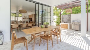 Un patio espacioso con mesa y sillas de madera, ventilador de techo y zona de barbacoa.