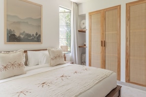 Relax in a serene bedroom with a large bed, framed landscape painting, and ample storage space.