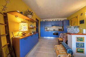 Een keuken met blauwe kastjes, een houten bankje en een eettafel met tafelkleed.