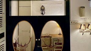 Una habitación con una puerta azul oscuro, dos espejos redondos, un reloj, una mesa de ajedrez y un letrero de Wi-Fi.