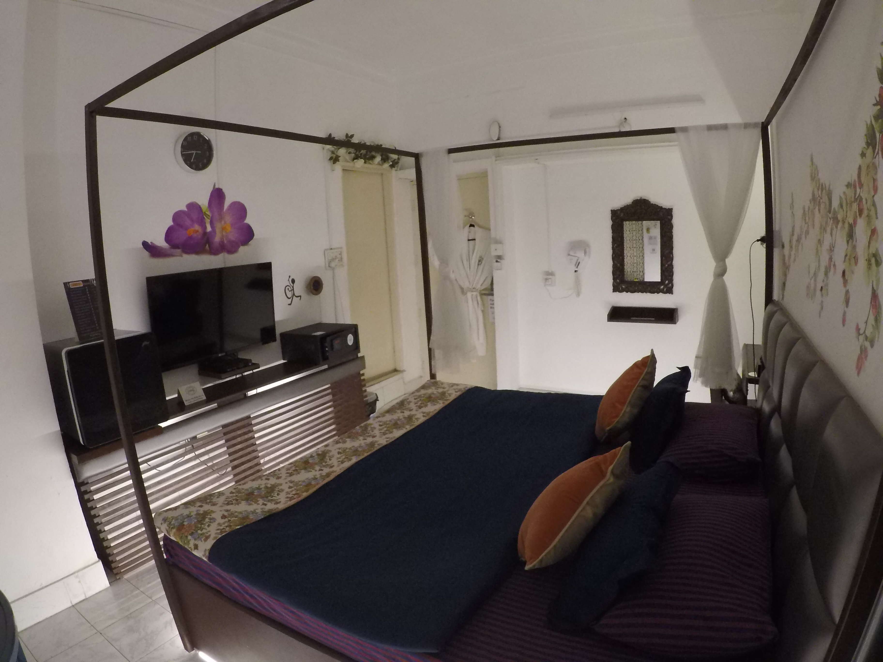 A bedroom with a bed, a TV, a mirror, and a window with curtains.