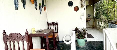 A patio with a wooden table and chairs, a potted plant, and decorative masks on the wall.