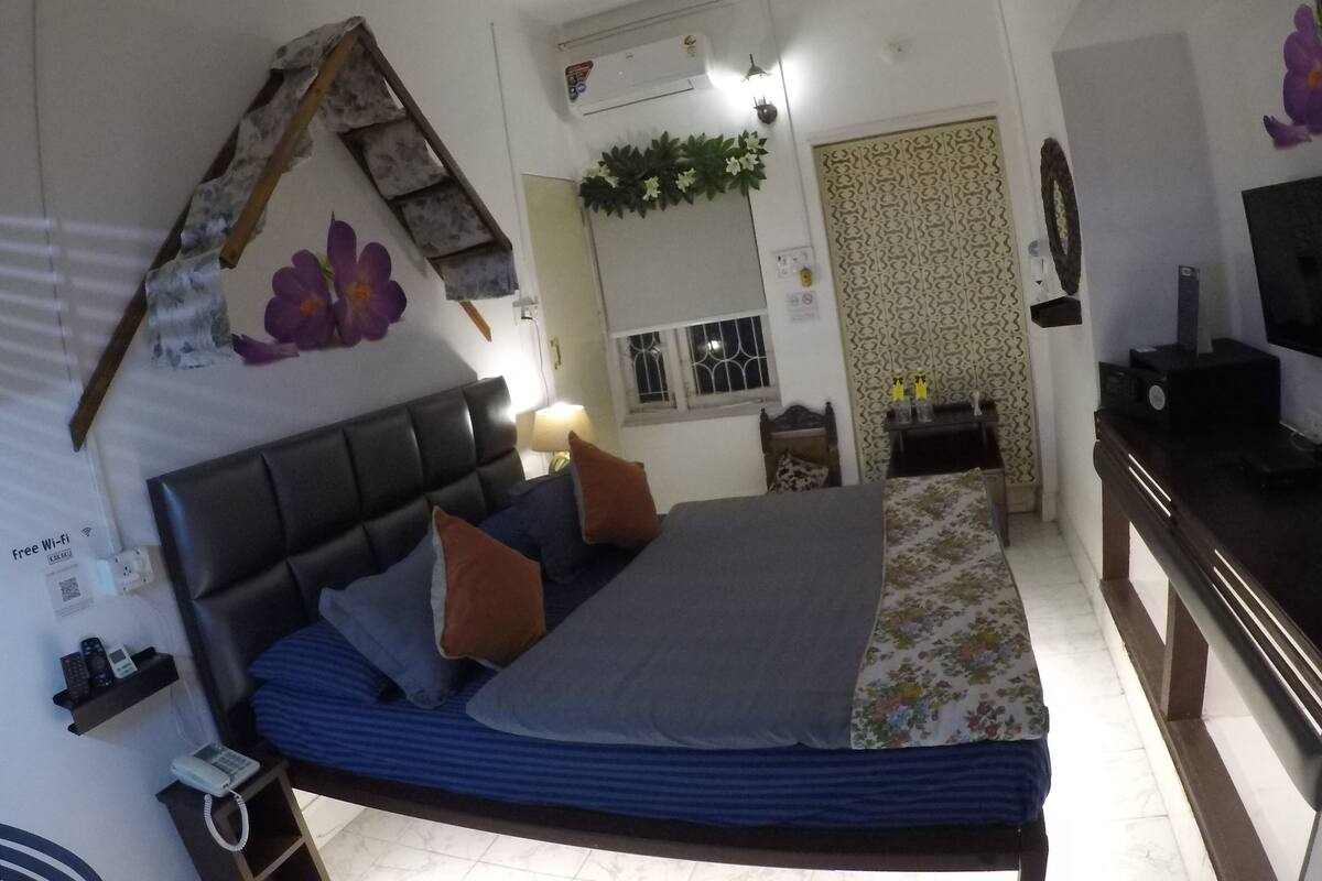 Een slaapkamer met een bed, een plafondventilator, een airconditioning, een televisie en een klein tafeltje met decoratieve objecten.
