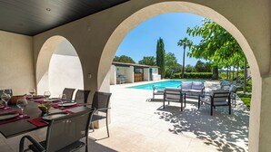 Eine Außenpatio mit einem Esstisch für vier Personen, ein Poolbereich mit Liegestühlen und Blick auf ein Gebäude mit einem Ziegeldach.