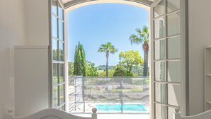 Ein Schlafzimmer mit großem Fenster, zwei Betten und Blick auf Pool und Grünflächen.