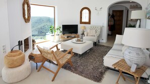 Uma sala de estar moderna com lareira, televisão, sofá e vista para o exterior.
