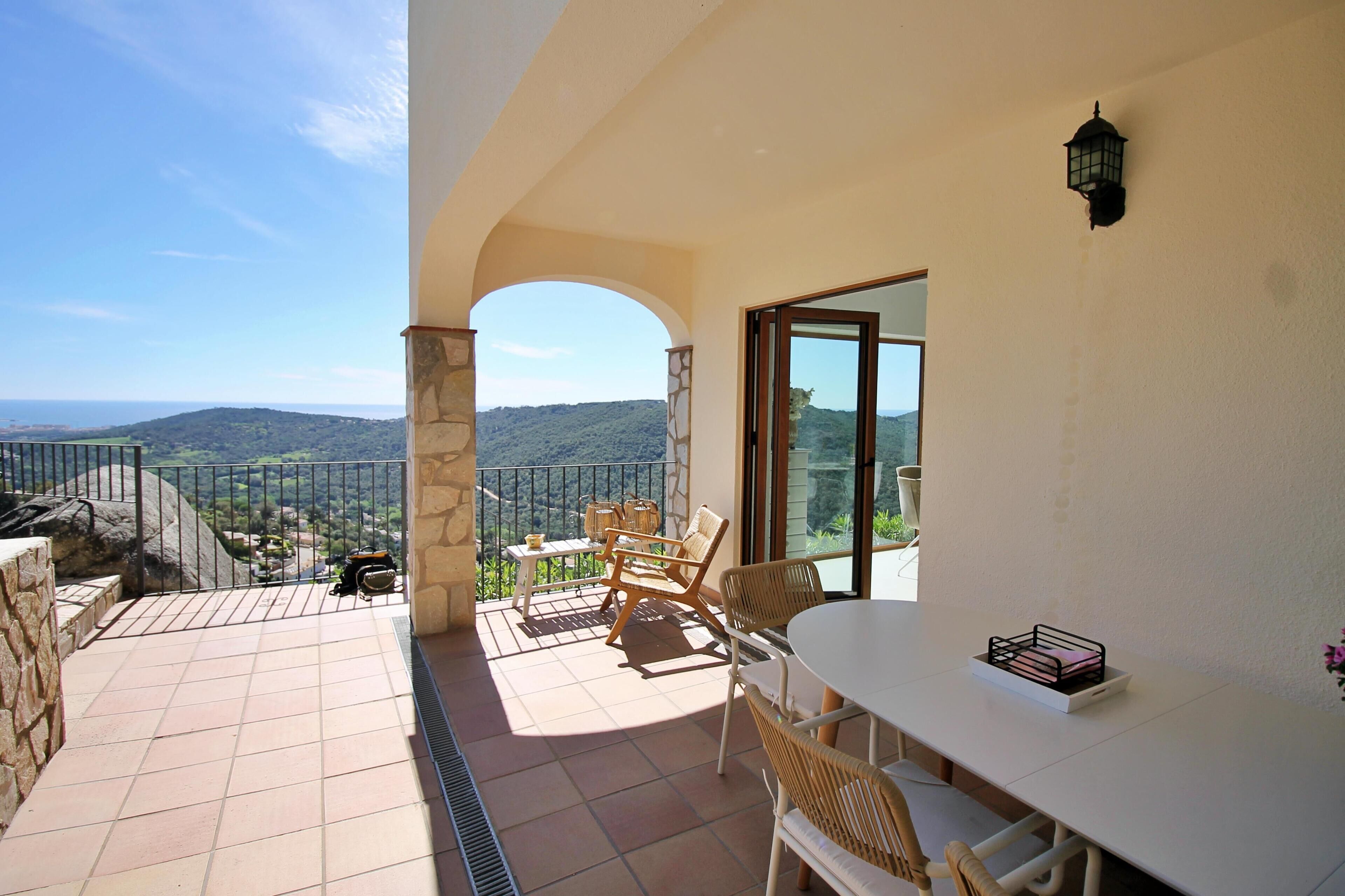 Un balcon avec une table et des chaises, un mur en pierre et une vue sur le paysage.