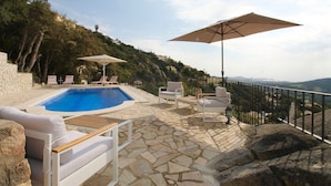 Uma área de piscina com piso de pedra, espreguiçadeiras e guarda-sóis.