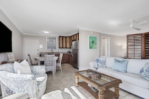 A modern living room with a white sofa, a glass coffee table, and a dining area with a white table and wicker chairs.
