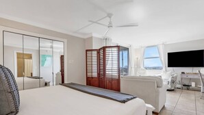 A hotel room with a bed, a TV, a desk, a chair, and a view of the city.