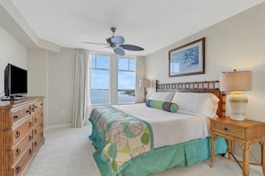 A hotel room with a bed, a television, a ceiling fan, a window with a view, and a painting on the wall. - Unforgettable Gulf, Estero Bay & Sunset Sky Views | 9th Floor Balcony | Heated Resort Pool & Hot Tub (Fort Myers Beach)