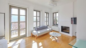A bright living room with large windows, a fireplace, and a glass coffee table.