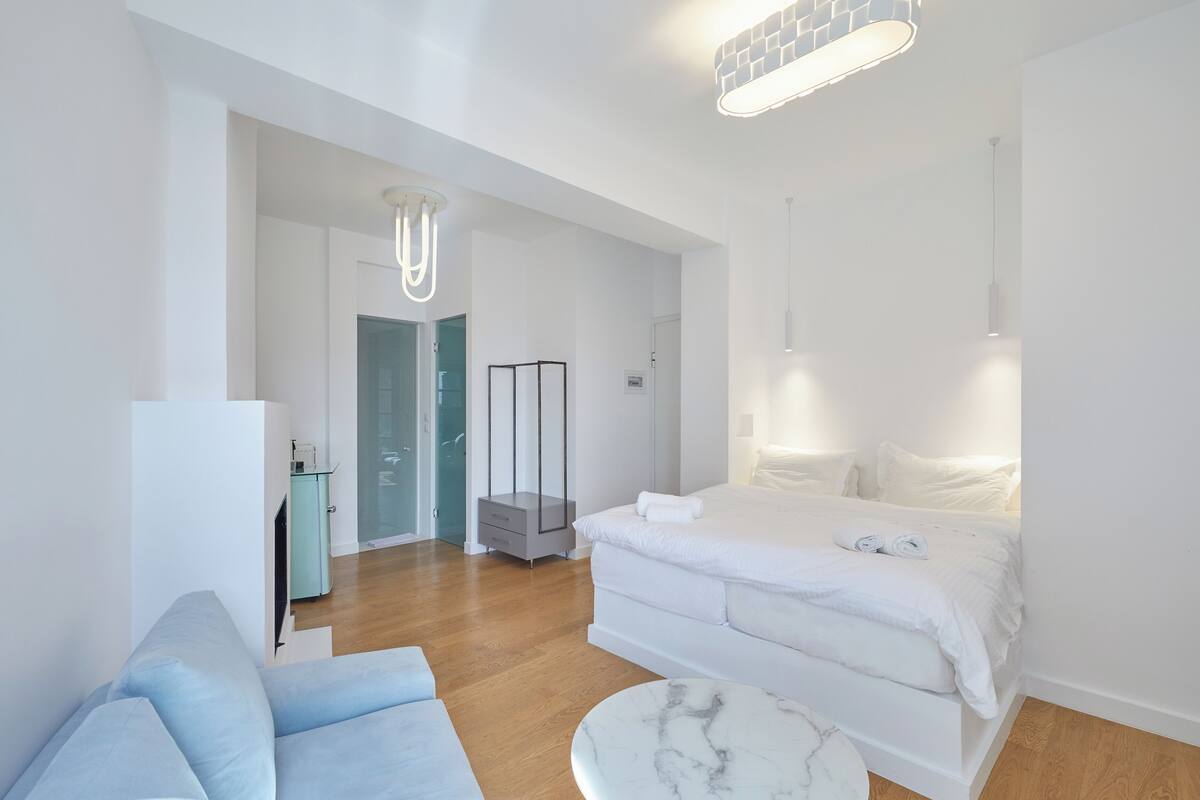 Une chambre moderne avec un grand lit, un canapé, une table basse en marbre et un dressing.