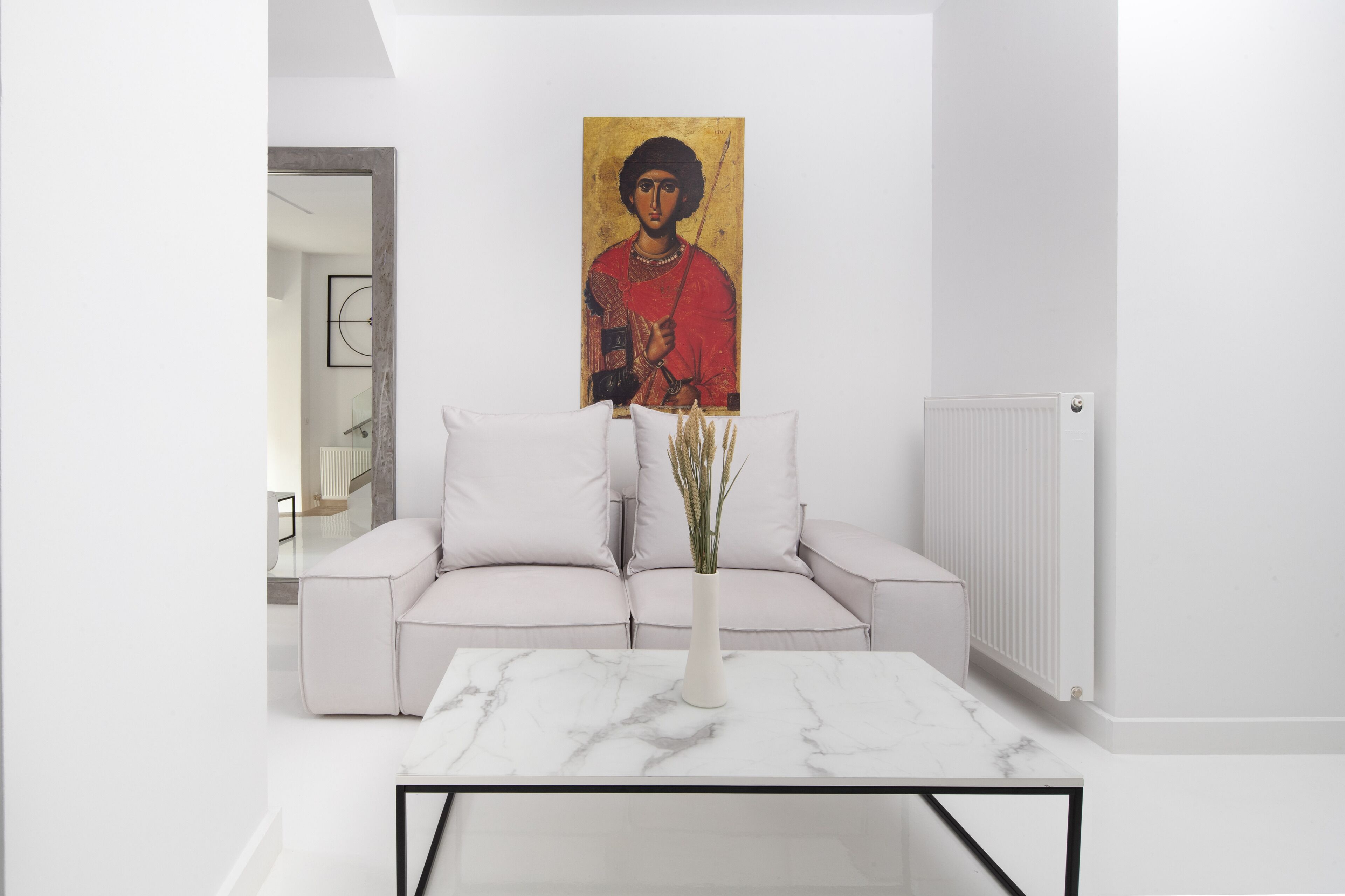 A modern living room with a white sofa, a marble coffee table, and a painting on the wall.