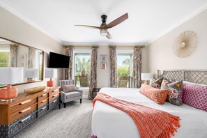 A bedroom with a bed, a desk, a chair, a television, and curtains.