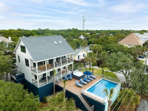 A two-story house with a large balcony, a swimming pool, and a lush green landscape.