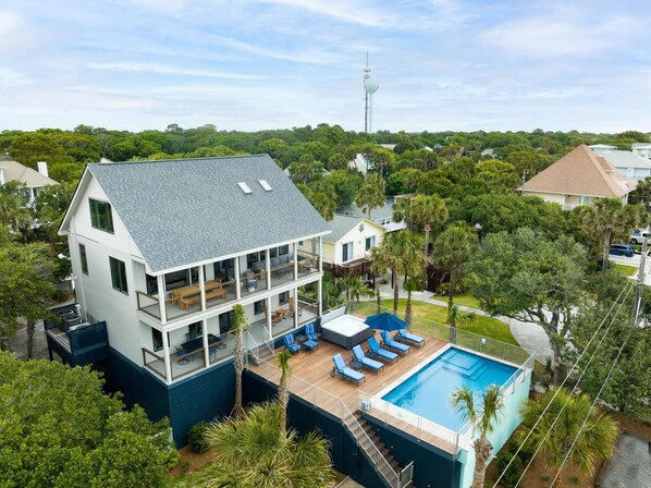 A two-story house with a large balcony, a swimming pool, and a lush green landscape.