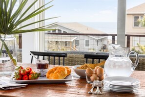 A breakfast table with a croissant, strawberries, a jam jar, eggs, and a pitcher of water.