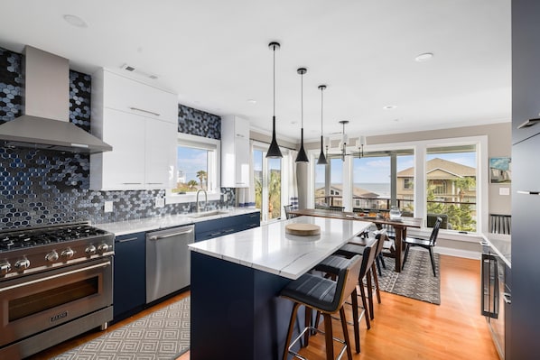 A modern kitchen with a central island, stainless steel appliances, and large windows.