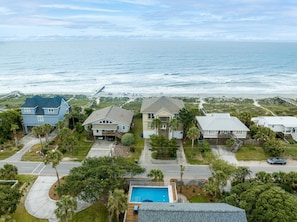 A coastal residential area with houses, a swimming pool, and a beach in the background.