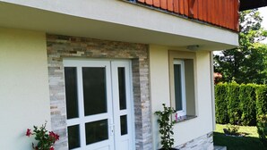 Una casa de dos pisos con balcón, fachada de piedra y entrada pavimentada.