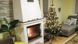 Una sala de estar acogedora con chimenea, un árbol de Navidad, una mesa de comedor con frutero y galletas, y un sofá.