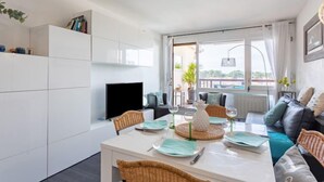 A modern living room with a dining area, white cabinetry, a flat-screen TV, and a large window with a view. - mille sabords by Interhome (Capbreton)