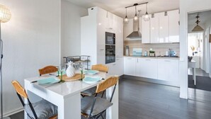 A modern kitchen with white cabinets, a dining area with a white table and chairs, and pendant lighting. - mille sabords by Interhome (Capbreton)