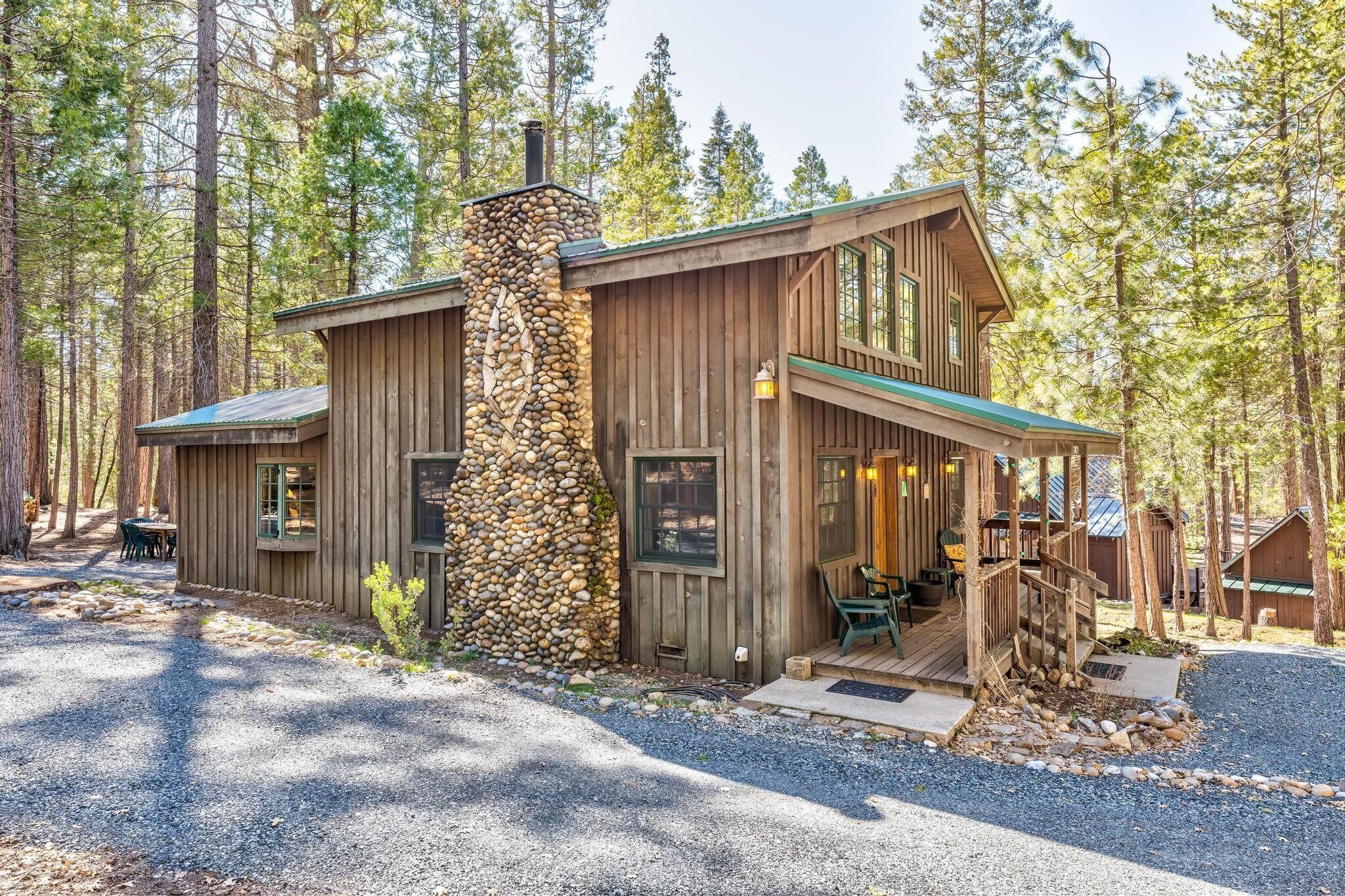 Une cabane rustique dotée d’une cheminée en pierre, d’un revêtement extérieur en bois et d’une véranda avec des sièges d’extérieur.