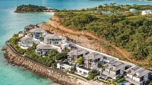 A coastal residential area with houses along a rocky shoreline, connected by a bridge. - Panorama Suite – Oceanview Luxury Suite at Tamarind Hills, Antigua (Unknown)